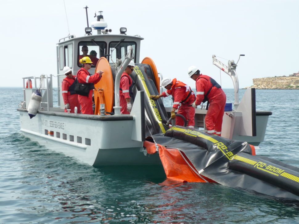 Oil spill response crew and vessel deploying boom into sea